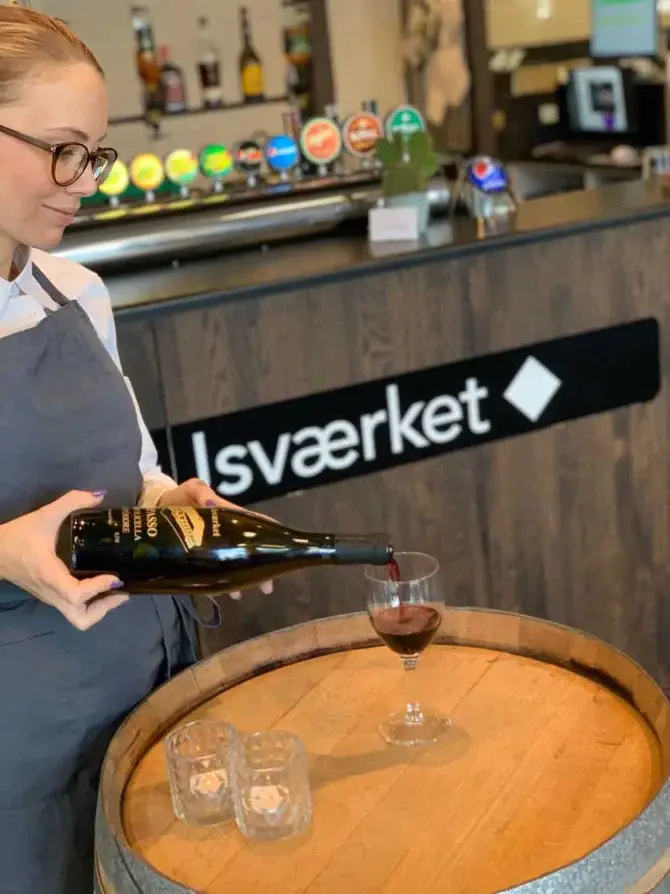 Bartender skænker rødvin på træfad ved baren.